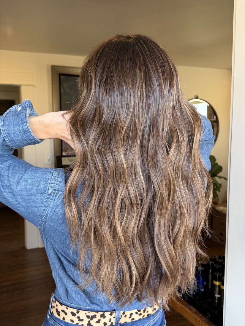 Rich dimensional brunette with caramel ribbons through the lengths, worn with a denim shirt.