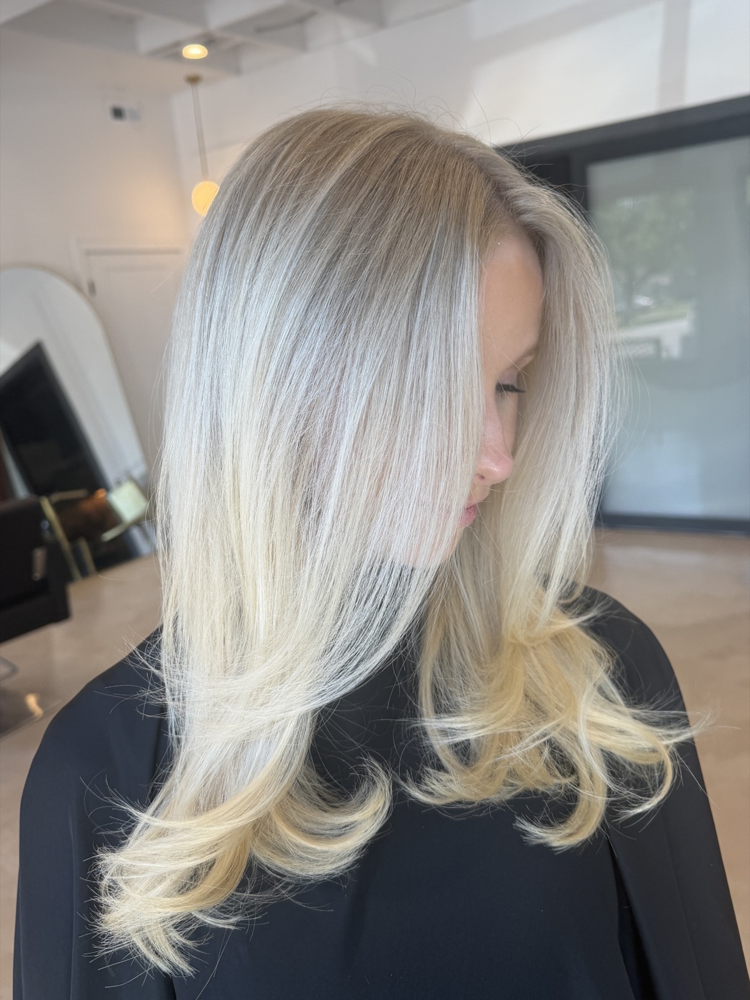 Icy platinum with softly curled ends, side profile, dark salon cape.