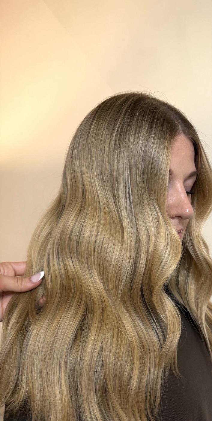 Warm golden blonde waves against a cream backdrop, face partly turned away.